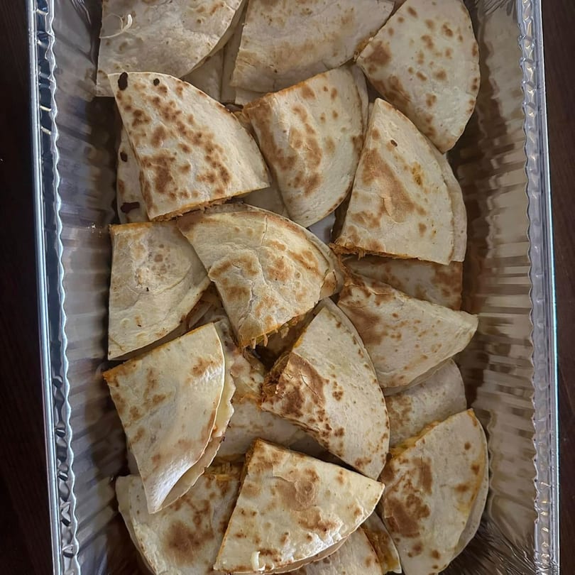 A catering tray filled with many triangular pieces of El Sazon Mexican Grill quesadillas.