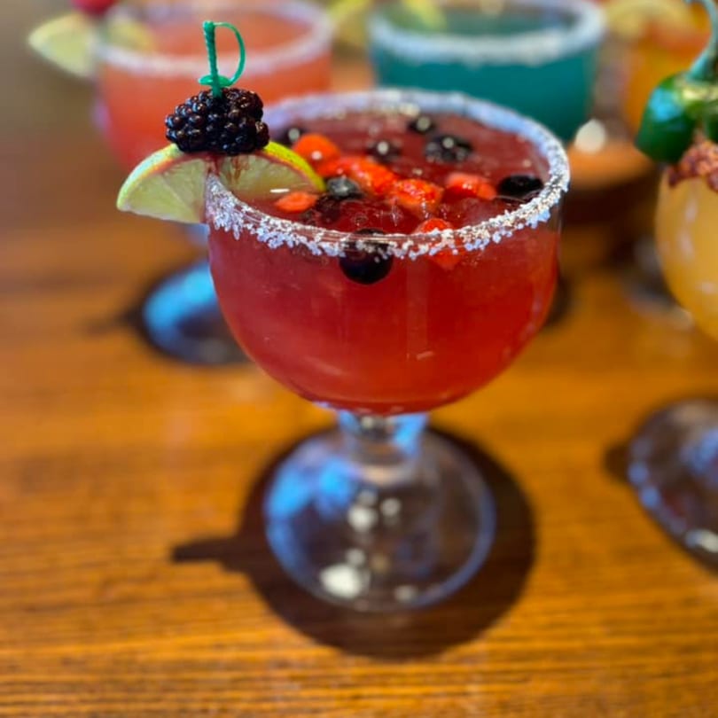A vibrant red berry margarita with a salted rim, lime, and blackberry garnish on a wooden table.