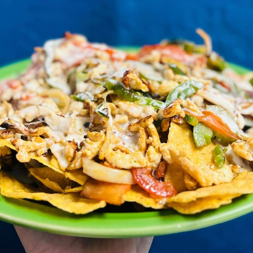 A vibrant plate of El Sazon Mexican Grill nachos, topped with chicken, peppers, onions, and creamy sauce.