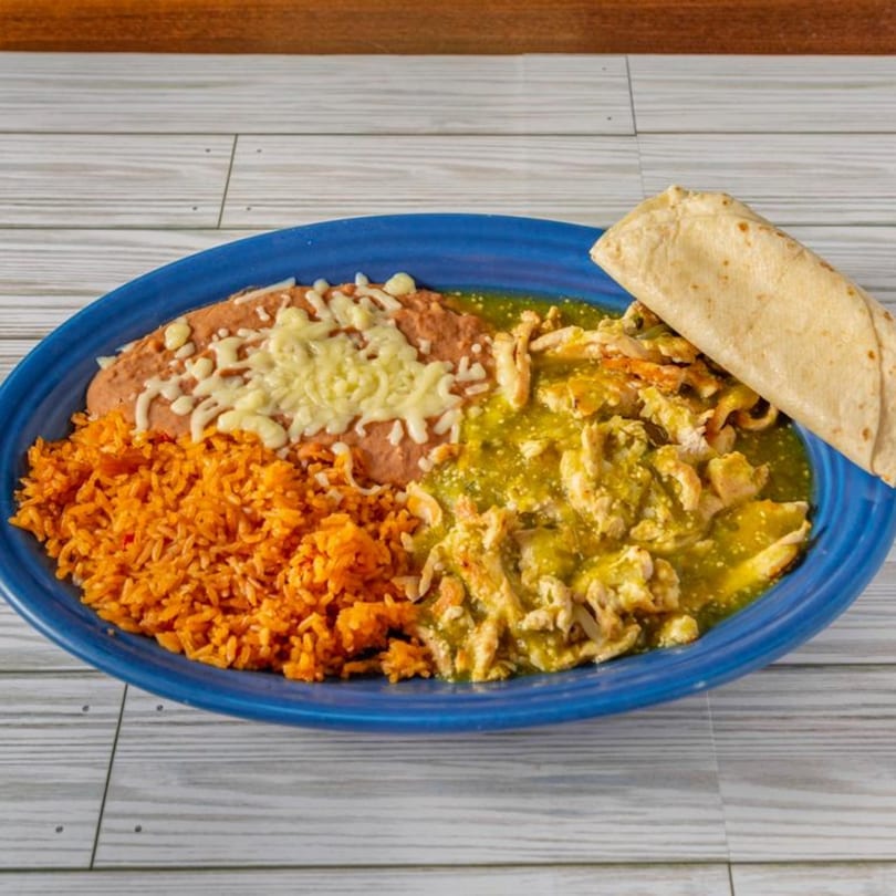 A blue plate with Mexican rice, refried beans with cheese, and chicken in green salsa, with a tortilla.