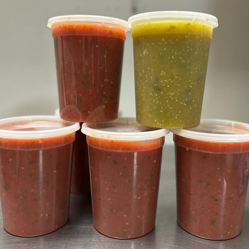 Five clear plastic containers of El Sazon Mexican Grill's red salsa and one green salsa.