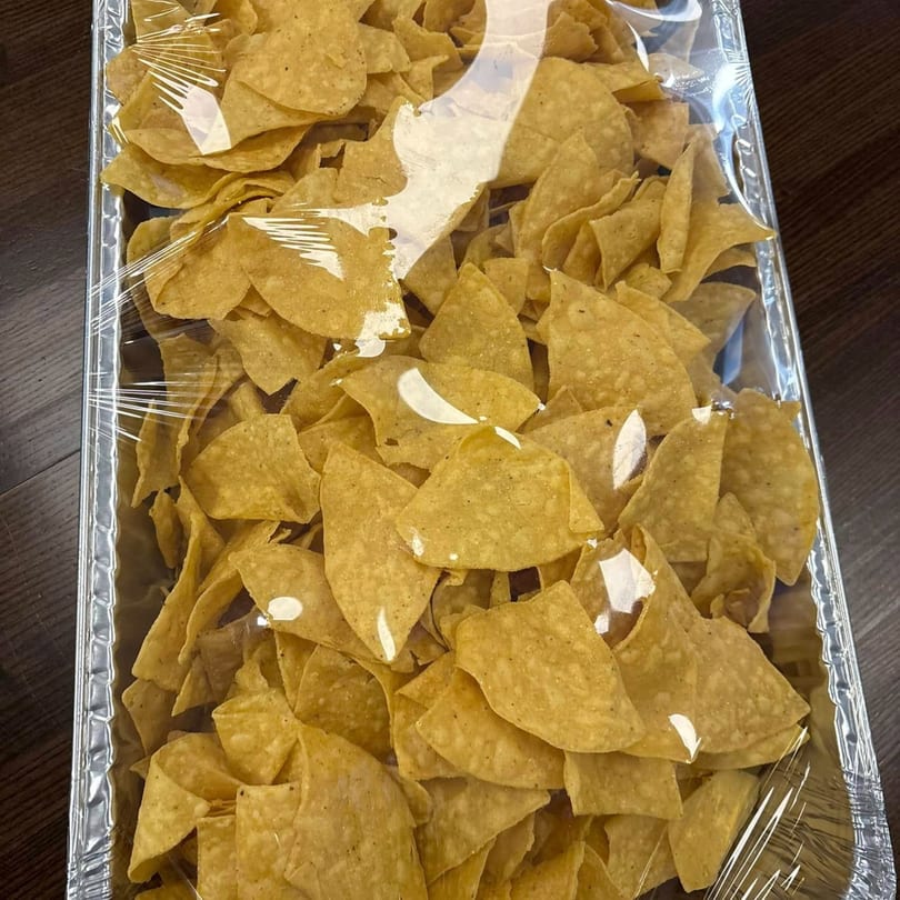 A catering tray of crispy tortilla chips, covered in clear plastic wrap, from El Sazon Mexican Grill.