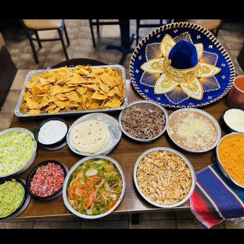 A catering spread of Mexican food, including chips, meats, rice, beans, and a sombrero.
